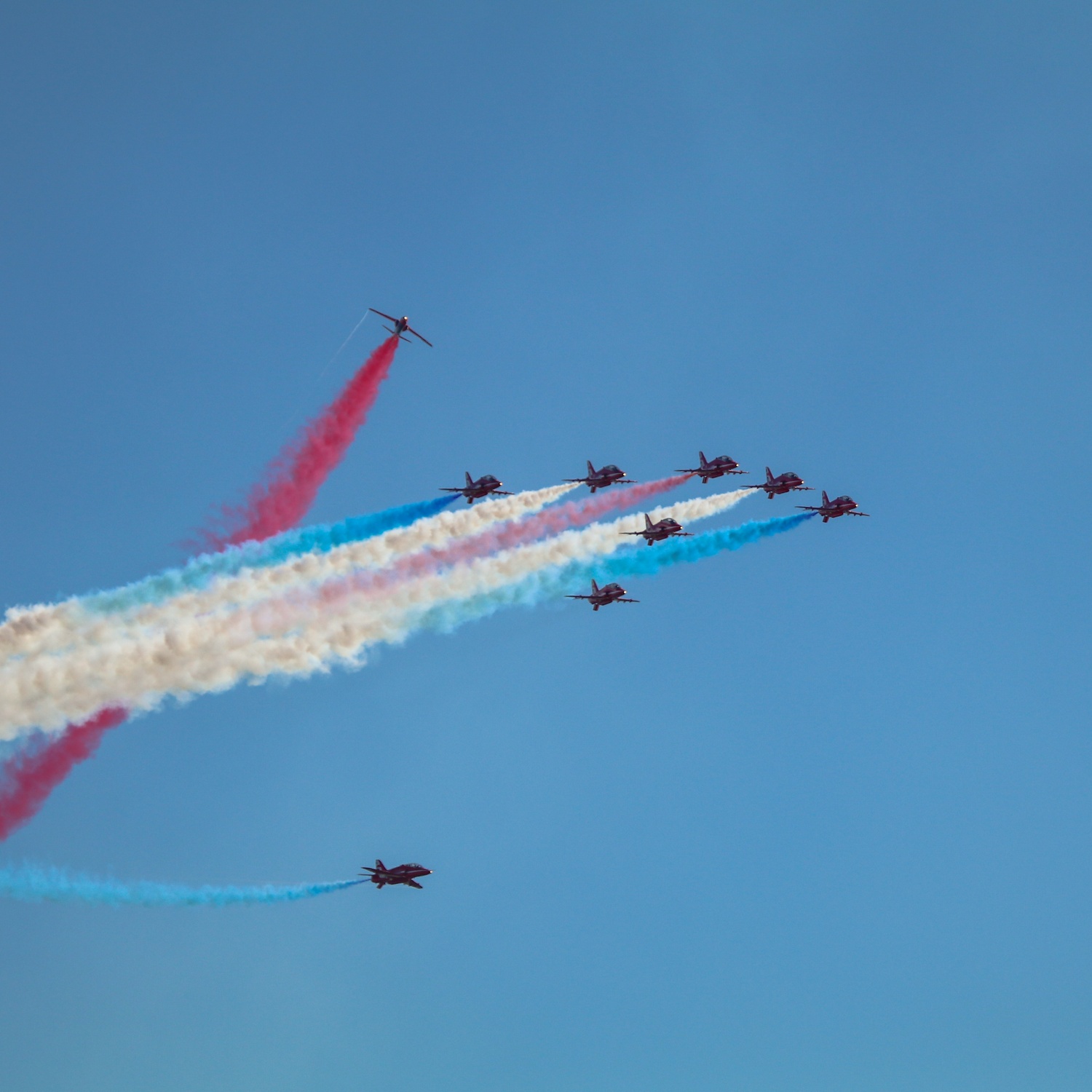Red arrows performing a formation flypast with two planes looping around with smoke trails against clear blue sky