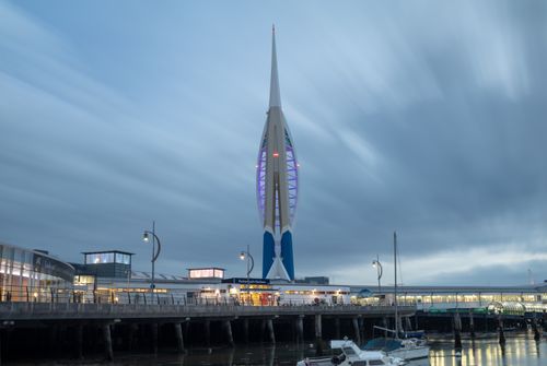 Spinnaker Tower viewed from behind in Portsmouth Harbour at low tide. Clouds are elongated by the long exposure.