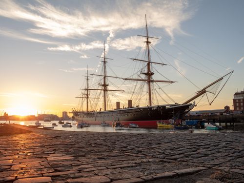 HMS Warrior in Portsmouth Harbour at low tide with the setting sun behind. Slipway in the foreground.