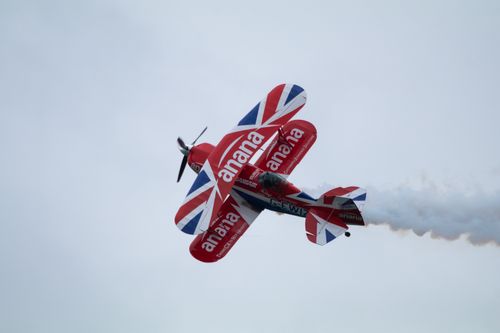 Super Pitts Muscle plane in bright red white and blue union flag livery, flying sideways at an angle using the fuselage as a lifting body against a grey sky