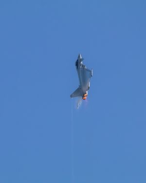Eurofighter Typhoon flying vertically with afterburners on against blue sky. The is a contrail from the tip of the rudder and wingo vapour forming on wings.