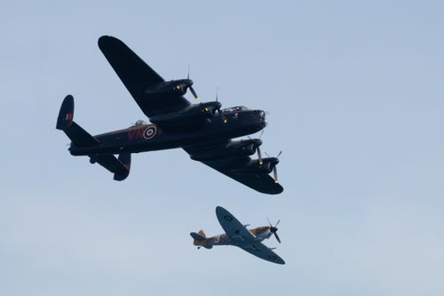 Lancaster bomber and Spitfire flying in formation against blue sky