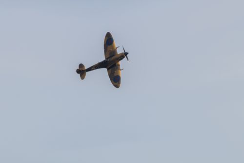 Spitfire making curve towards camera with top of wing visible against blue sky. The aircraft is in a sandy dessert camouflage livery