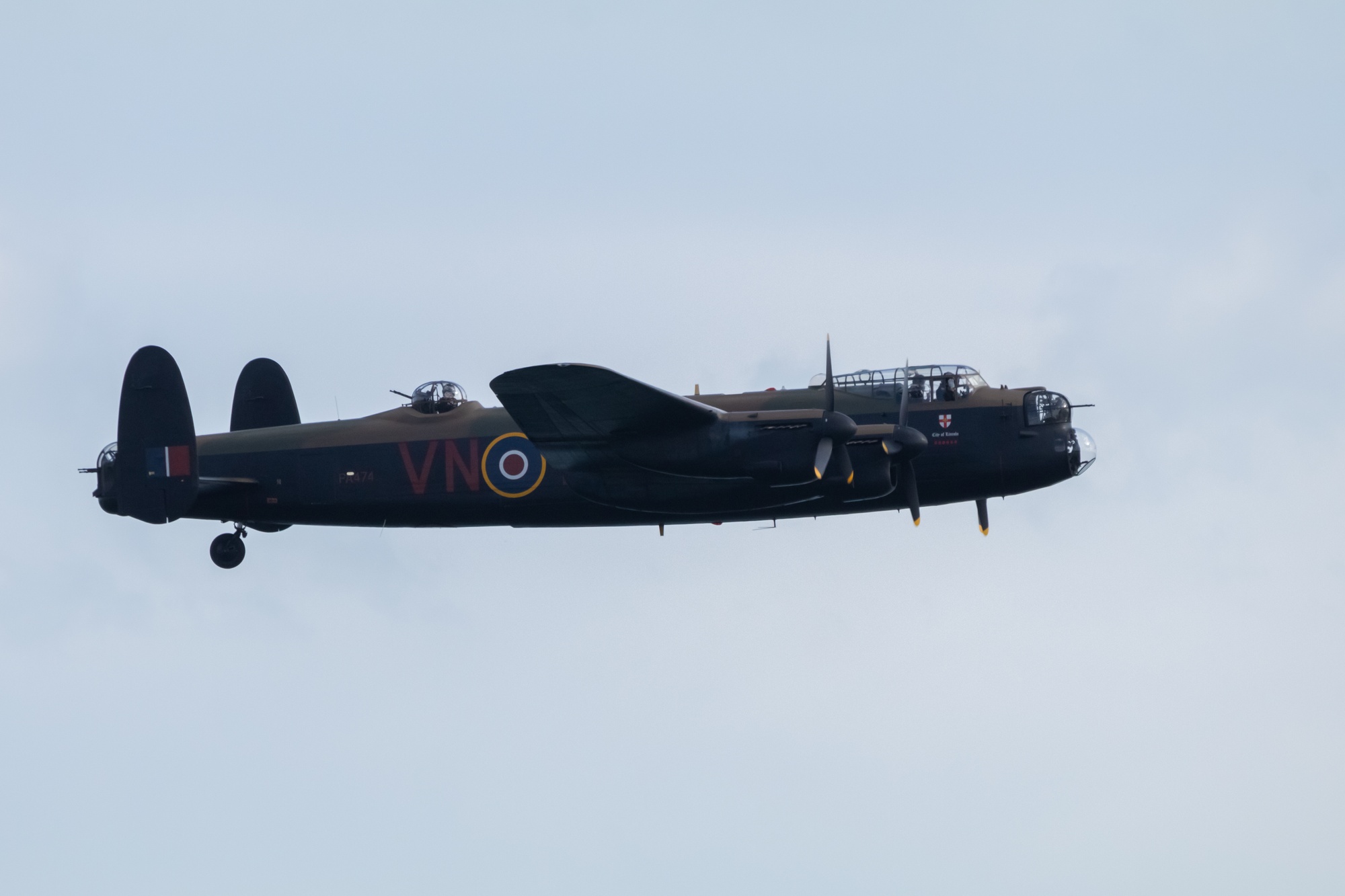 Lancaster bomber dipping its wings towards the camera allowing for a side profile of the aircraft. All cockpits are manned.