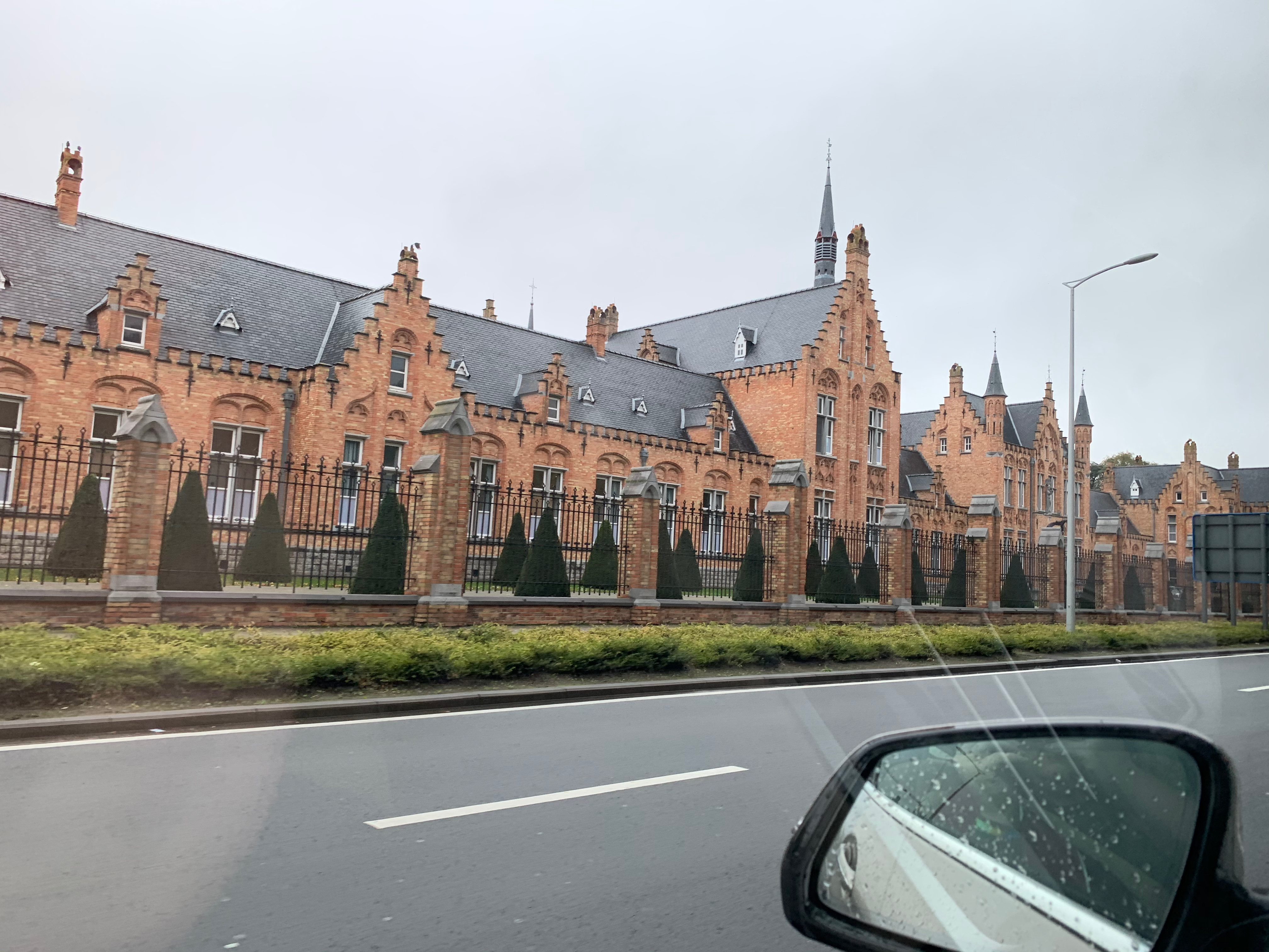 Large orange brick building along roadside. The photo is taken from within a car with the wing-mirror visible in the bottom left