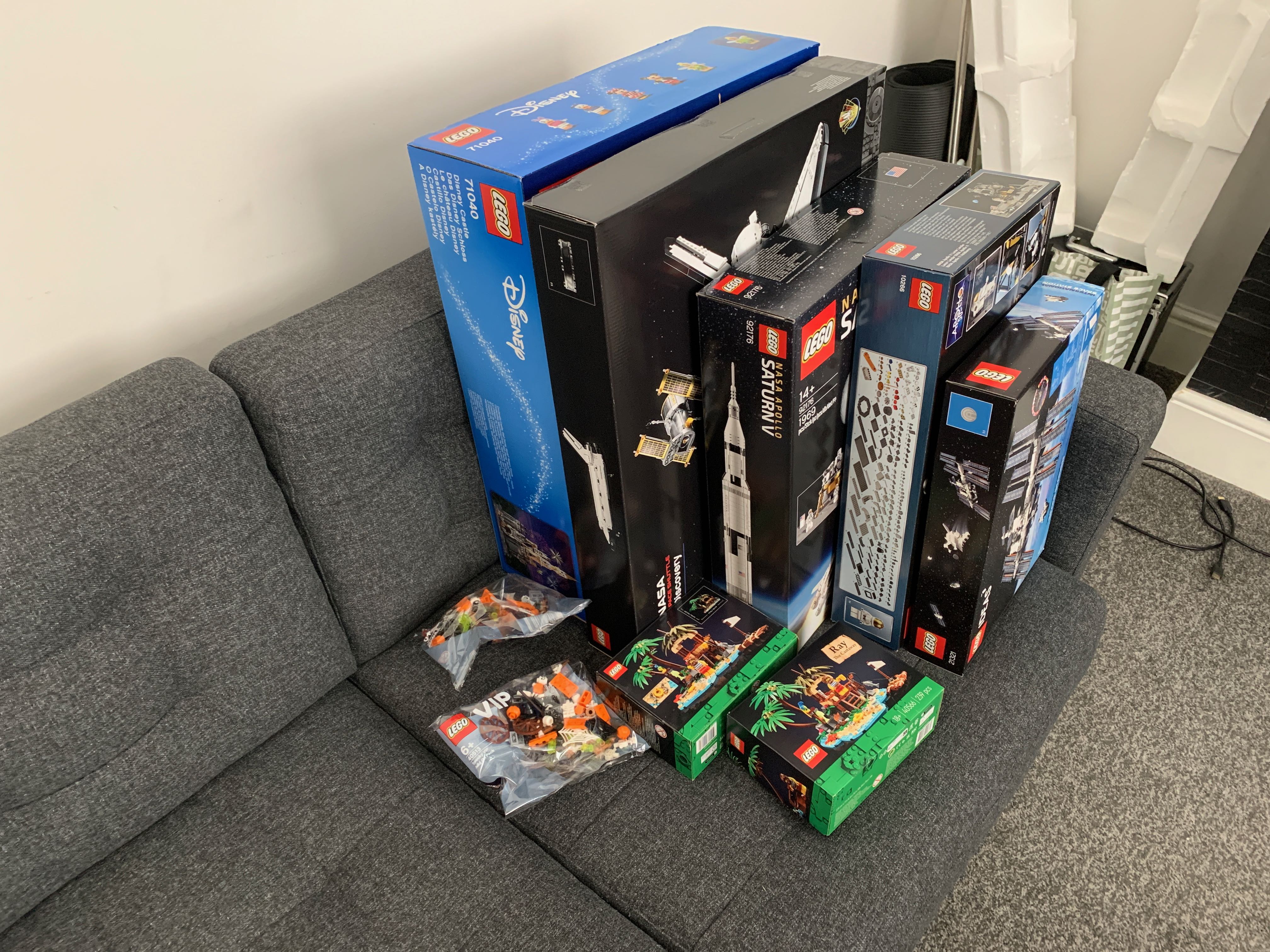 Lego Disney Castle, Space Shuttle Discovery, Saturn V, Apollo Lander, ISS boxes sat on a sofa 