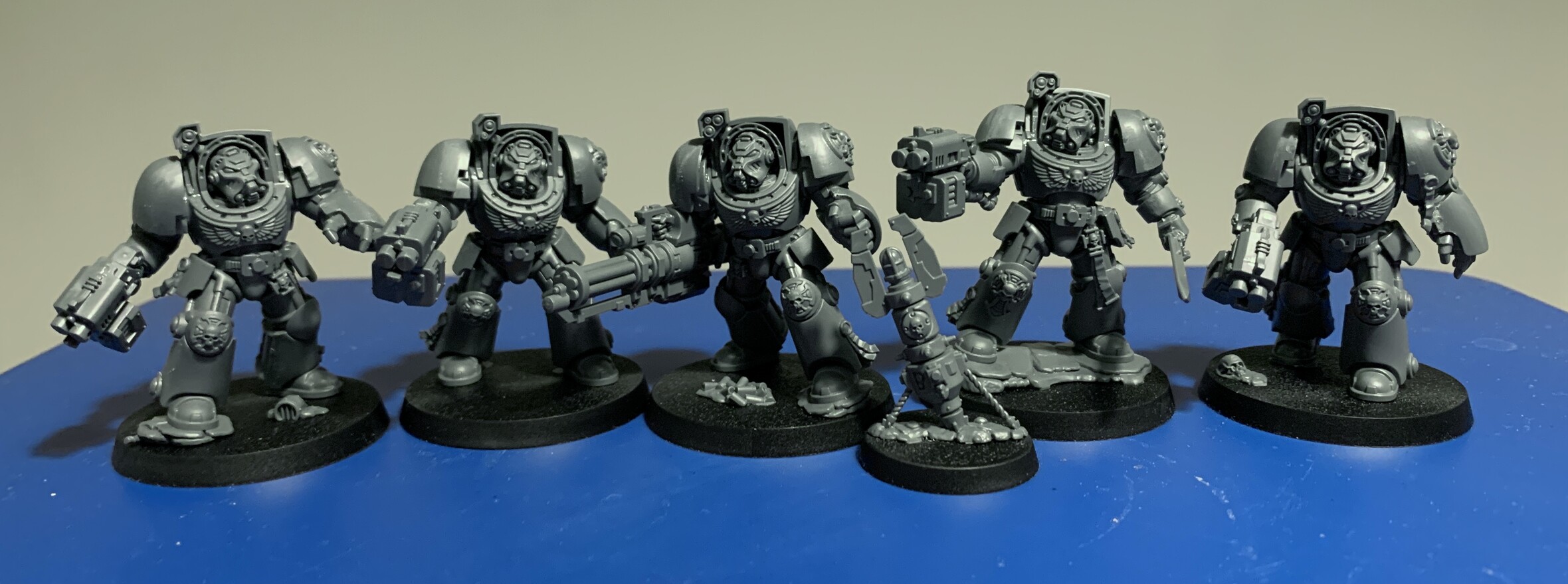 5 of the new larger Warhammer 40k terminator space marine models with a homing beacon in front. They have assortment of weapons with most carrying dual barrelled weapons. One has a large barrelled mini-gun style weapon and one is carry a sword. The homing beacon looks like a missile that’s landed and lodged in the ground.