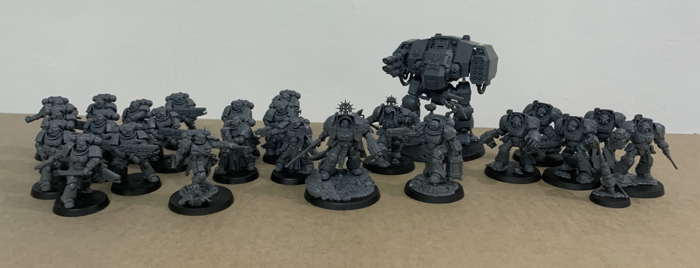 Multiple Space Marines and a dreadnought on a cardboard tray. From left to right are 10 infernos marines, a lieutenant, 5 sternguard veterans, a Captain in terminator armour, a Librarian in terminator armour, a apothacary biologus in gravis armour, a Ballistus dreadnought and 5 terminators with a homing beacon
