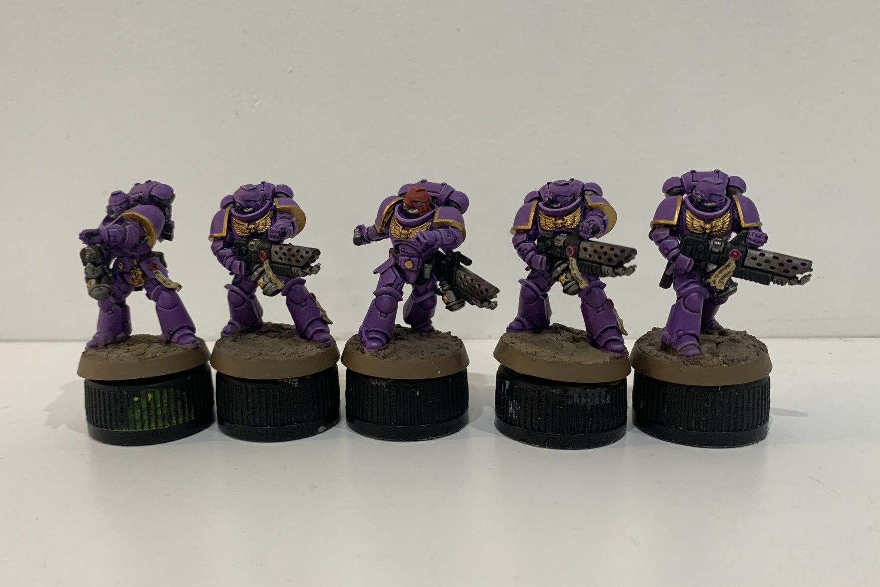 Five Infernus Space Marines standing side by side. Their main armour is painted in a pinky-purple colour scheme with gold trimming. The four outer Marines are holding flame weapons with the central marine throwing a grenade.