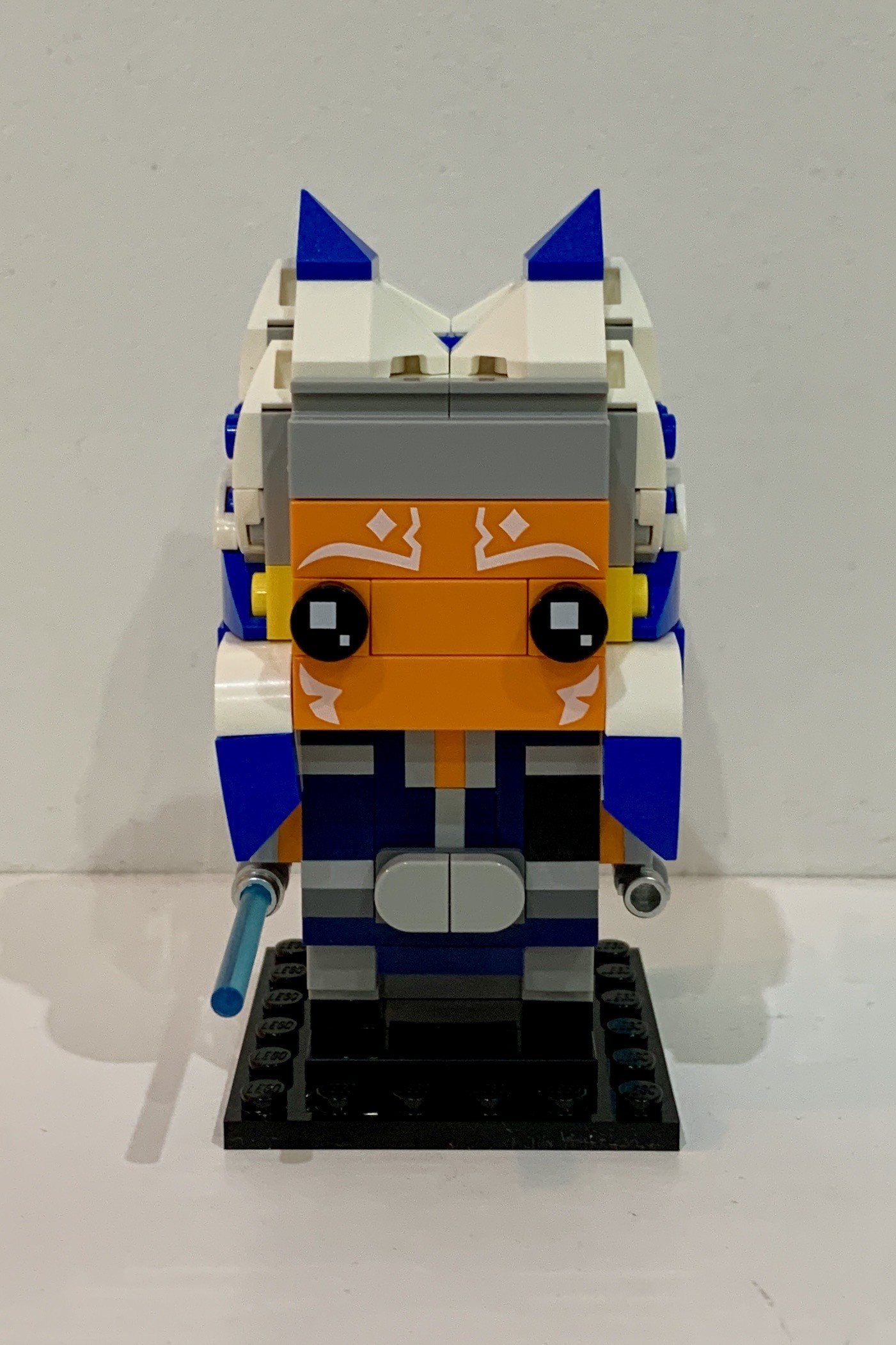 Lego BrickHeadz Ahsoka Nano from Star Wars. She is a humanoid with orange skin, white face marking and blue and white hair. She is wearing dark blue clothes and carrying two light blue light sabres.