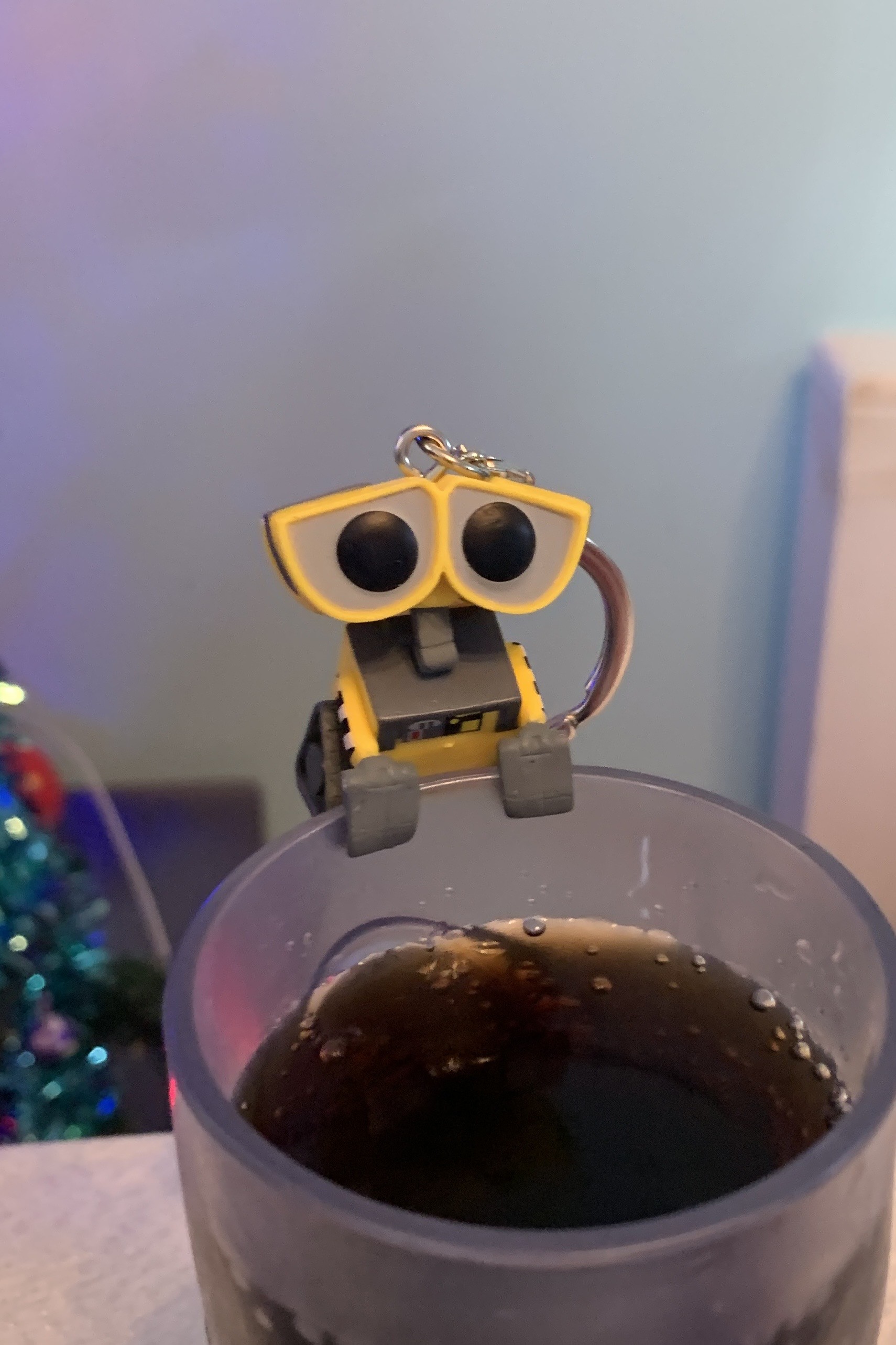 A small WALL-E from Disney using his grippers to hold onto the edge of a glass filled with coke