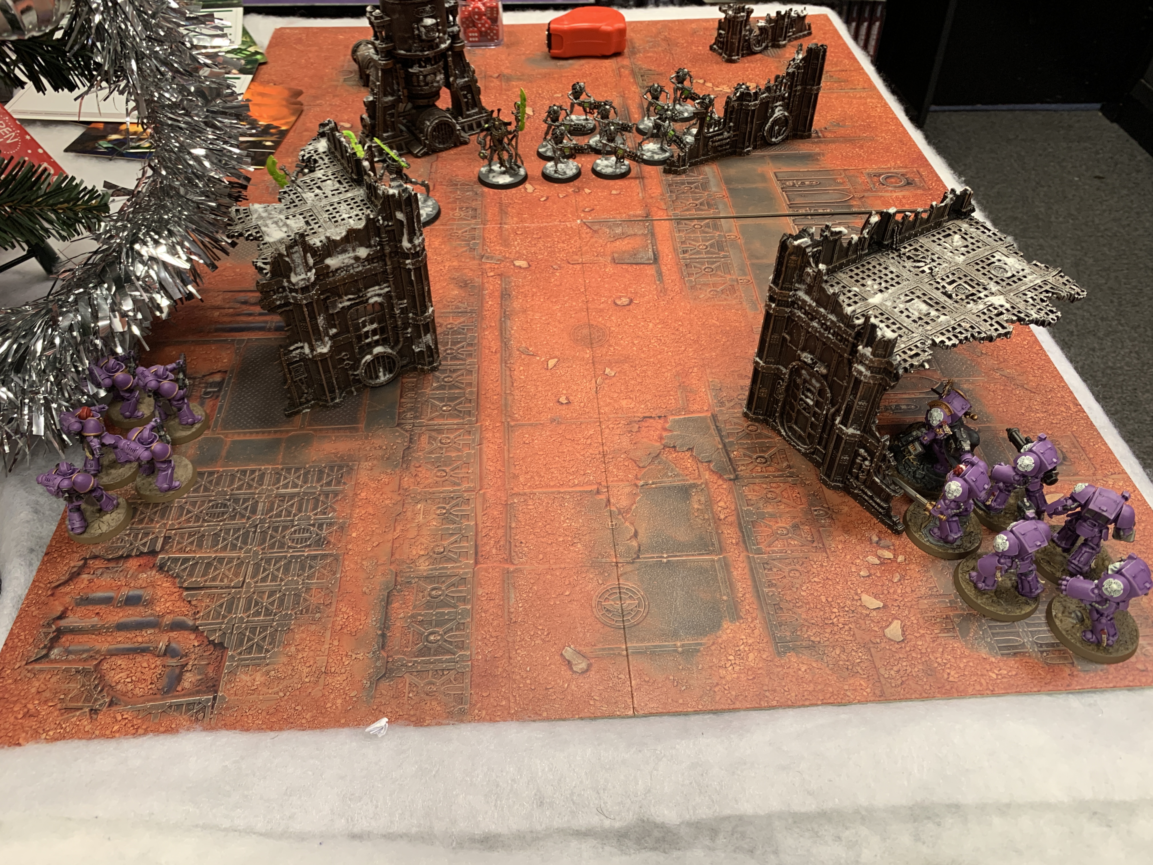 A battlefield with various bits of terrain. In the bottom right corner is six purple Space Marines in Terminator Armour hiding behind a ruin. At the bottom left are five purple Infernus Marines hiding behind a ruin. In the centre are ten Necron Warriors and a Necron Overlord.