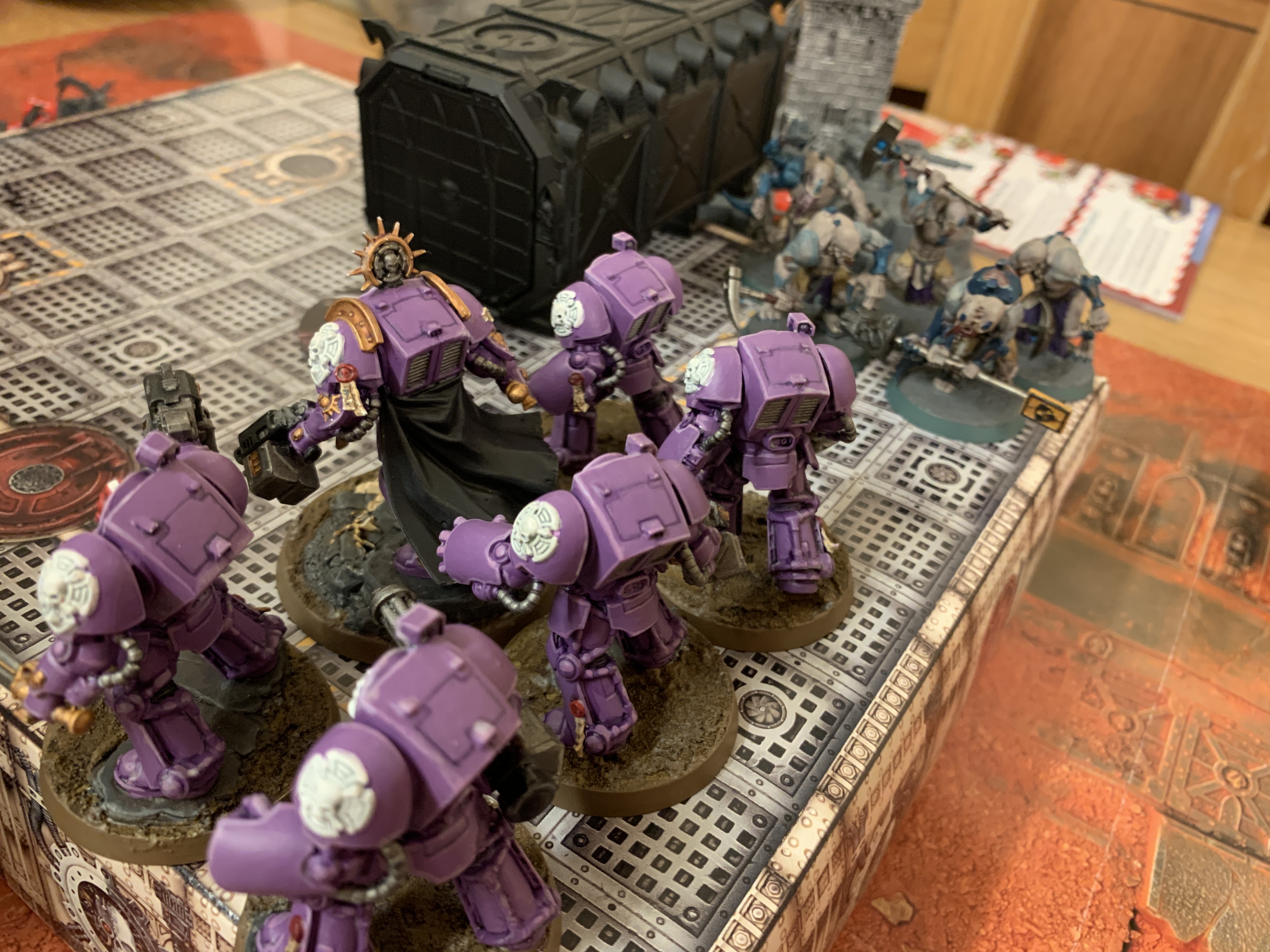 5 purple Space Marines in Terminator Armour facing left with 5 Aberrants approaching them holding various improvised weapons including a road sign
