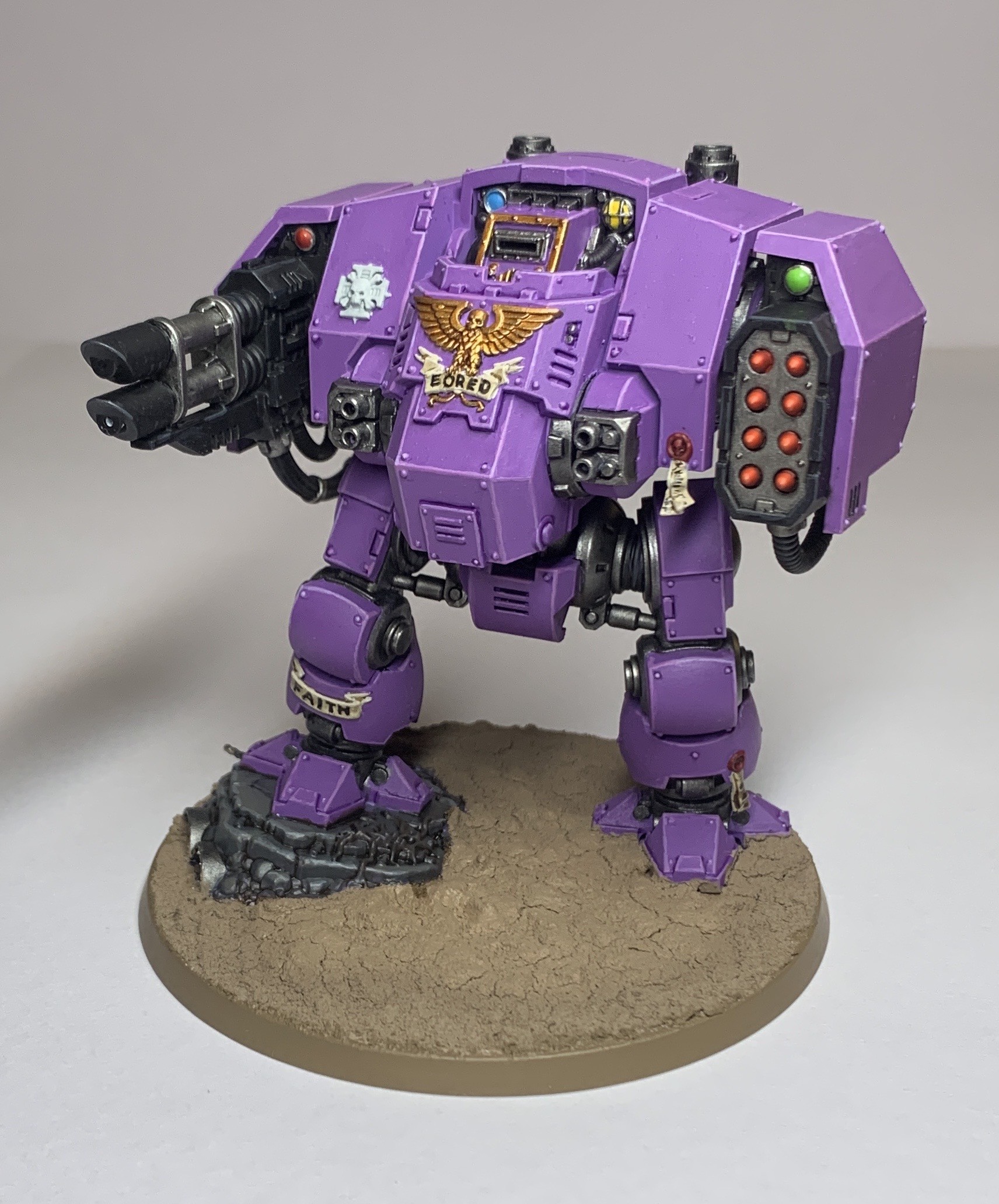 Purple Space Marine Balistus Dreadnought stood on a barren soil base. The dreadnought is a bipedal robot with its arms replaced with a pair of lascannons on its right and a missile launchers on its left. The centre of the body has a golden eagle and a scroll saying Eored, and the it’s right shin has a scroll saying FAITH.