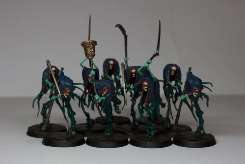 Ten tall blue green ghosts with dark blue capes, with various weapons. Their bodies are a dark blue green while their arms are a ghoulish green, their heads are pale bone. The heads are encircled by a long red ribbon that also covers their eyes. All of them except the leader is holding a long scythe in various states of disrepair and rust. The leader is holding a large brass bell on a wooden stick 