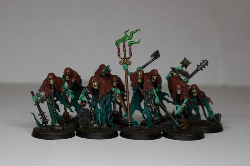 Ten blue green ghosts with red brown capes, with various weapons. Their bodies are a dark blue green while their arms are a ghoulish green, their heads are pale bone. Most have various rusted and damaged weapons, the one in the centre is holding a candle stand with pink candles and pale green flames. They are all stood on muddy bases  